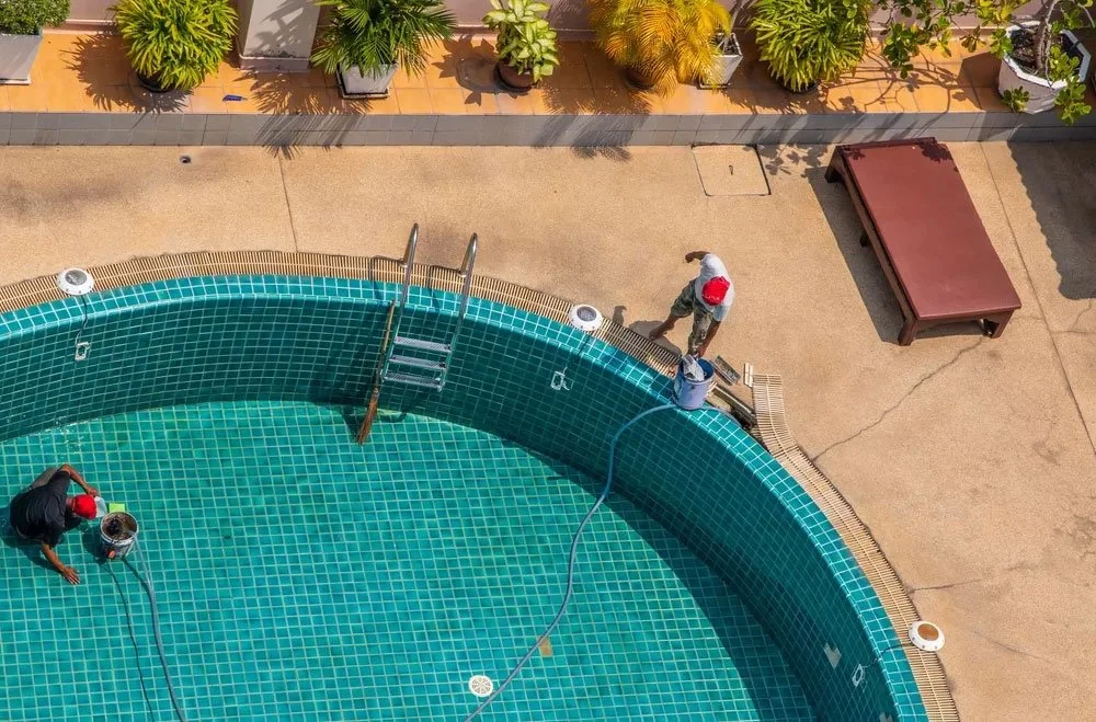 Two workers cleaning a swimming pool with buckets and hoses, from an aerial view.