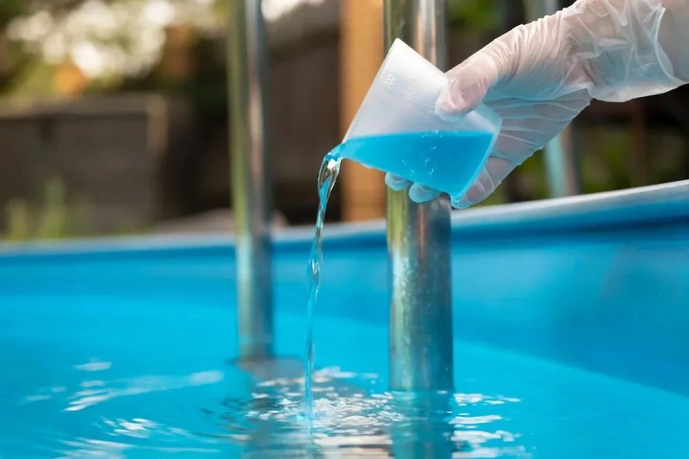 Person wearing gloves pouring blue liquid into a pool.