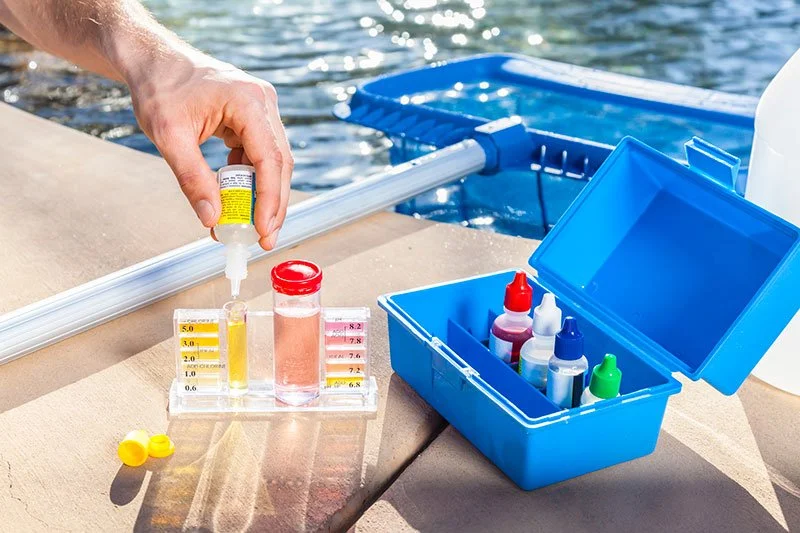 Collection of water testing supplies on a dock, including test bottles, chemicals, and a color comparison chart.