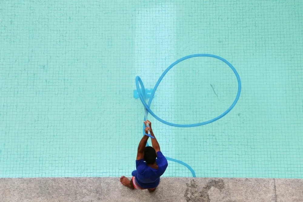 A person cleaning a swimming pool with a hose.