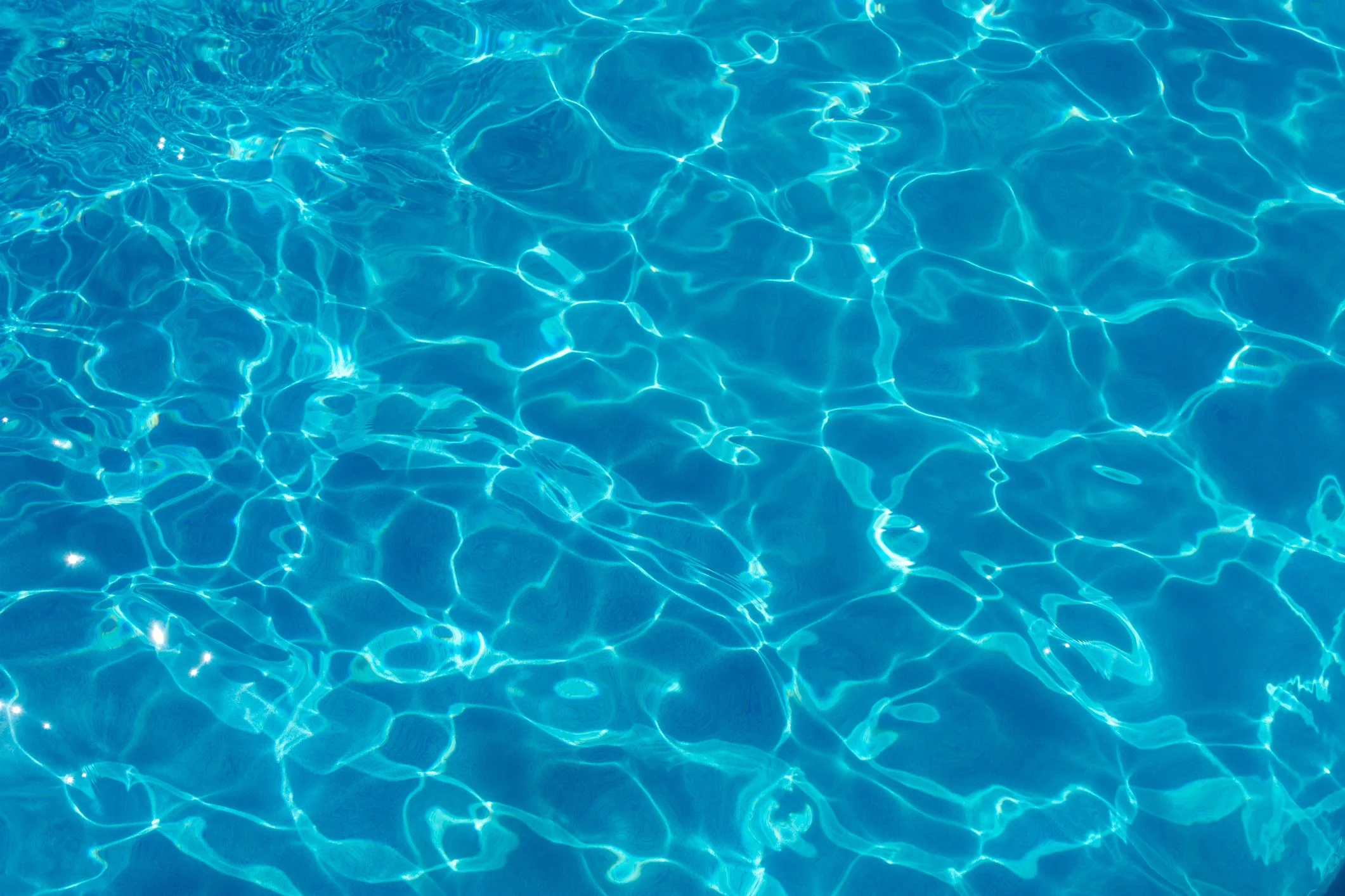 Clear blue water in a swimming pool with ripples and light reflections.